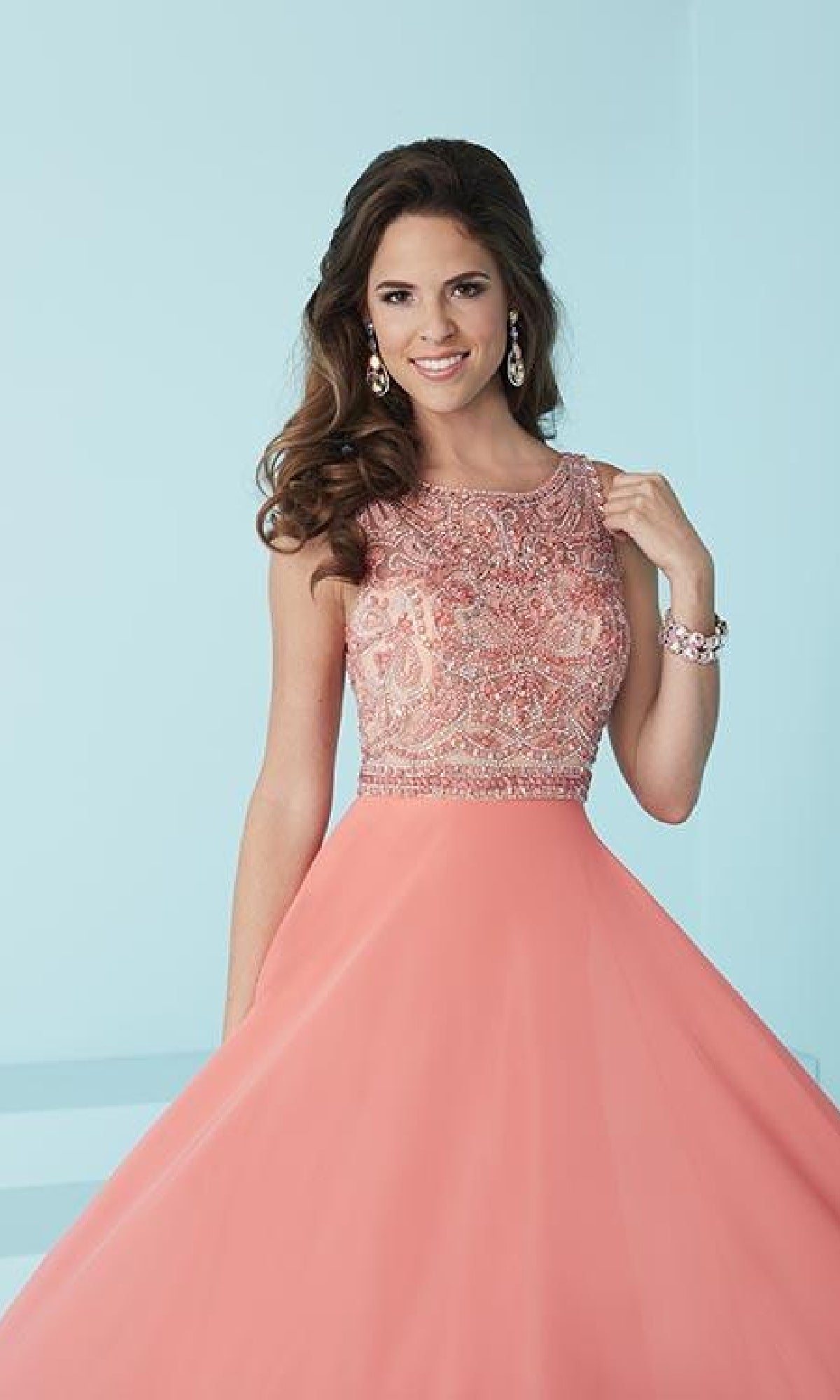 A woman poses against a light blue background wearing the Backless Long A-Line Formal Gown, featuring a sleeveless design, coral pink color, embellished bodice, and flowing skirt.